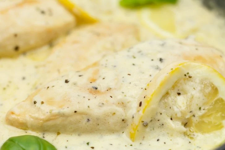 Chicken in creamy lemon sauce served on a plate with fresh herbs