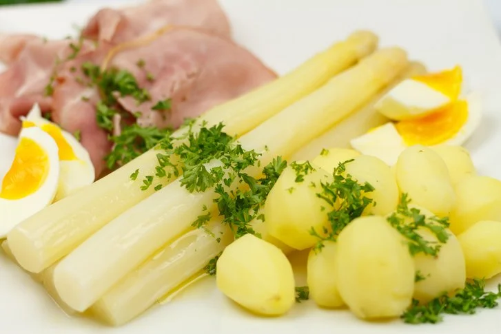 Witte asperges met ham en botersaus op een bord