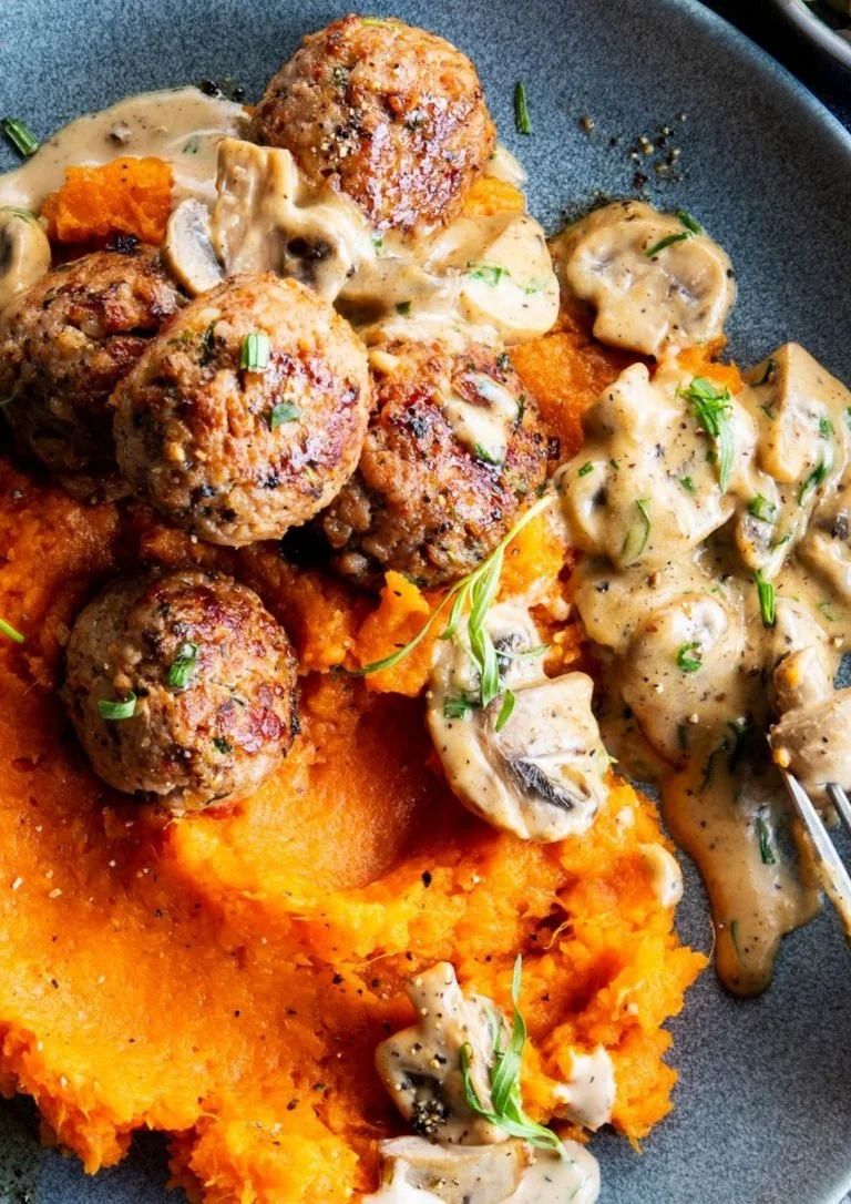 Vleesballen met zoete aardappelpuree en champignonsaus op een bord.