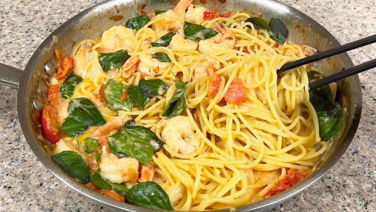 Een bord spaghetti met garnalen en romige saus, geserveerd met verse kruiden.