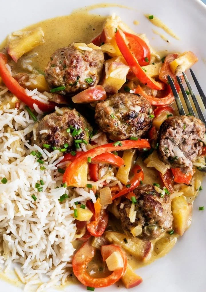 Balletjes in currysaus met rijst, appel en paprika op een bord