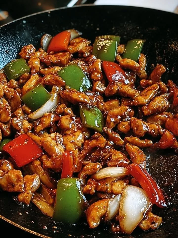Zwarte peper kip met paprika en gekarameliseerde uien in een wok.